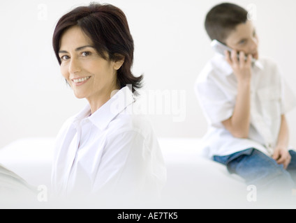 Reife Frau, Lächeln, junge im Hintergrund mit Handy Stockfoto