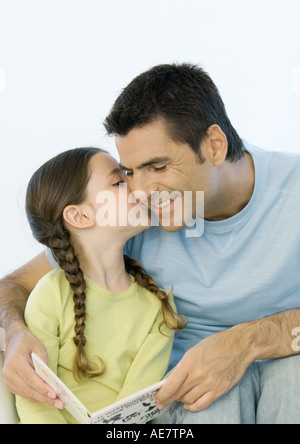 Mädchen des Vaters Wange küssen, während er Buch hält Stockfoto