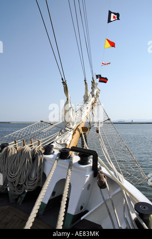 Der Bug des ecuadorianischen Großschiffs Guayas, mit gerollten Vorsegeln auf dem Bugspriet, Signalflaggen und gewickelten Anlegeseilen, mit Blick auf den Hafen von Cagliari, Sardinien, Italien. Stockfoto