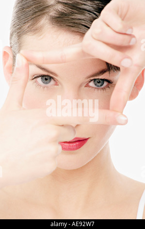 Junge Frau Gesicht mit Make up, schaut in die Kamera macht ein Frame mit ihren Fingern, Nahaufnahme (Studio) Stockfoto
