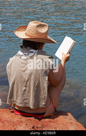 Junge Spanierin sitzt auf einem Felsen am Meer, das Buch zu lesen. Stockfoto