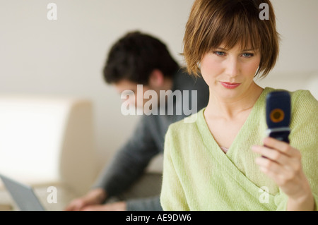 Frau mit Handy, Mann mit Laptop-Computer im Hintergrund Stockfoto