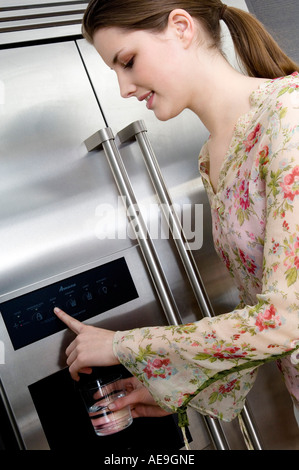 Junge Frau, die Wasser aus einem Kühlschrank Wasserspender in ein Glas gießen Stockfoto