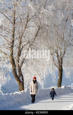 Mutter und Kleinkind zu Fuß draußen an kalten Wintertag unter frostigen Bäumen Oulu, Finnland Stockfoto