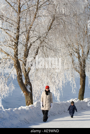 Mutter und Kleinkind zu Fuß draußen an kalten Wintertag unter frostigen Bäumen Oulu, Finnland Stockfoto