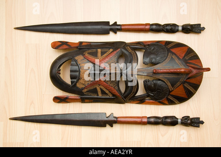 Afrikanische Maasai Mare Gesichtsmaske aus Holz. Geschnitzt aus schwarz und rot gefärbtem Holz mit braun-gelb verzierten Markierungen, mit zwei kurzen zeremoniellen Speeren. Stockfoto