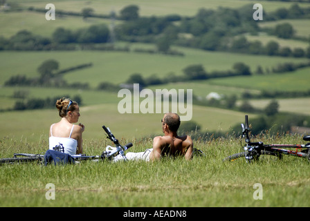 MÄNNLICHE WEIBLICHE RADFAHRER SITZEN UND GENIEßEN SIE DIE LÄNDLICHE AUSSICHT MIT BLICK AUF DIE SUSSEX DOWNS TEUFEL DYKE EAST SUSSEX Stockfoto