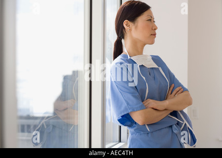 Asiatische Ärztin Fenster gelehnt, mit verschränkten Armen Stockfoto