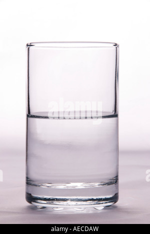 Ein Glas, das halb voll oder halb leer ist, um die Idee von Pessimismus oder Optimismus auf einem einfachen Hintergrund zu veranschaulichen Stockfoto