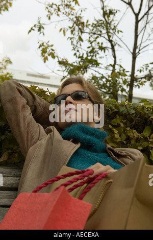 Junge Frau Sonnenbrille auf ruht auf Bank holding Einkaufstaschen Stockfoto