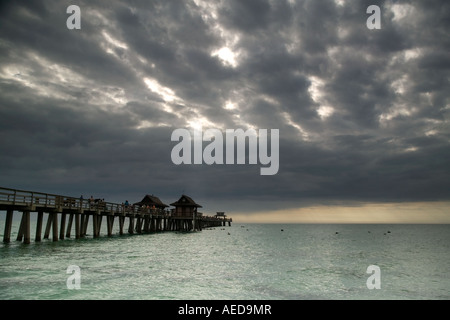 Die alte hölzerne Pier am Strand von Naples mit dramatischen stürmischen Himmel und Sonnenstrahlen über dem Meer Stockfoto