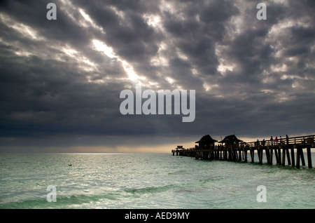 Die alte hölzerne Pier am Strand von Naples mit dramatischen stürmischen Himmel und Sonnenstrahlen über dem Meer Stockfoto