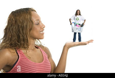 Eine junge Frau hält eine Miniaturversion von sich selbst in der Handfläche von ihrer Hand tragen ein Papierkorb. Stockfoto