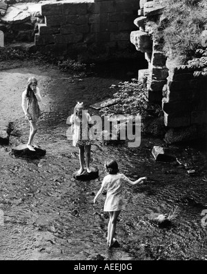 Vintage schwarz / weiß Drucken Scannen drei Mädchen spielen auf Trittsteine im Fluss bei Fountains Abbey in Yorkshire im Jahr 1973 Stockfoto