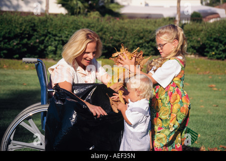 California, die junge Familie gemeinsam hilfreiche Unterstützung Hilfe Verletzten Verletzungen hilft Mutter junge weibliche Kinder setzen Herbst fallen Blätter Müllsack Stockfoto