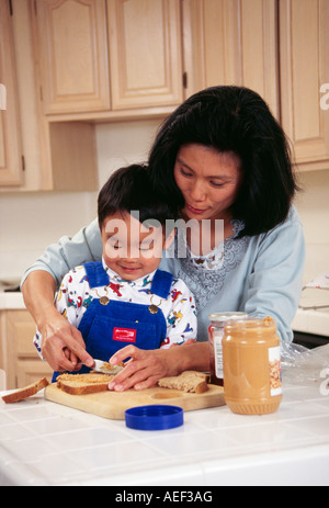 Japanische Mutter Sohn 2-3-jährige Anwendung Verbreitung Peanut Butter auf Brot lächelnd Rasse ethnische Herkunft ethnische Vielfalt ethnisch verschieden POV Myrleen Stockfoto