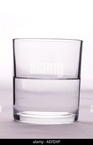 Ein Glas, das halb voll oder halb leer ist, um die Idee von Pessimismus oder Optimismus auf einem einfachen Hintergrund zu veranschaulichen Stockfoto