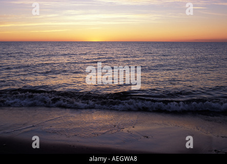 Welle rollt auf einem sandigen Strand bei Sonnenaufgang mit den Spitzen der Welle einfach brechen und fangen die Sonnenstrahlen s von hinten Stockfoto