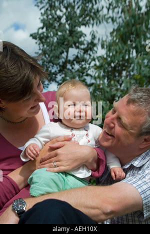 Vertikale Nahaufnahme Portrait einer jungen Familie (Mama, Papa und sechs Monate alten Erstgeborenen Tochter) im Garten. Stockfoto