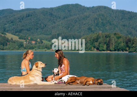 zwei Mädchen mit Dalmatiner, Hovawart Hund und halbe Rasse Hund am Bootssteg Stockfoto