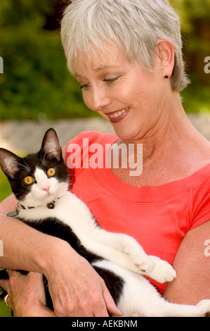 Porträt einer Reifen lächelnde Frau suchen Sie getröstet und glücklich hält eine schwarze und weiße Katze im Arm Stockfoto