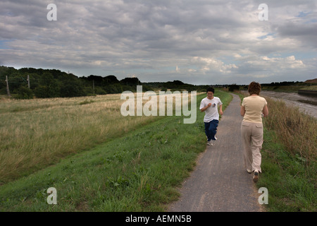 Ein Jogger führt vorbei an einer Frau, für einen Spaziergang auf einem einsamen Pfad entlang eines Flusses in Colchester Essex england Stockfoto