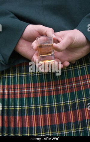 Mann trägt einen Tartan Kilt mit einem Glas Whisky hinter seinem Rücken bei Braemar, Ballater Highland Games. Stockfoto