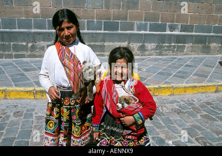Zwei junge Mädchen lächelnd, tragen bunte Kleidung hält ein Lamm und ein Hund in ihren Armen, Cusco, Peru Stockfoto