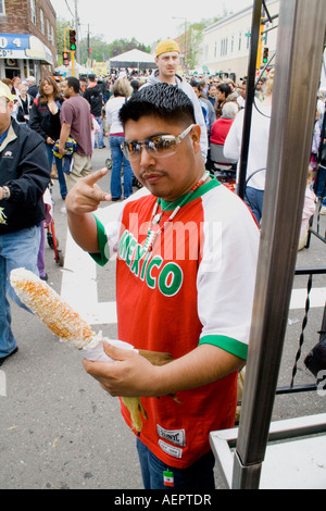 Chicano Mann mit 19 Jahren signalisiert wird, dass er frisch genießt, geröstete Maiskolben. Cinco De Mayo Fiesta. "St. Paul" Minnesota USA Stockfoto