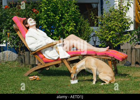 Frau auf Liegestuhl - junge halbe Rasse Hund trinken Stockfoto