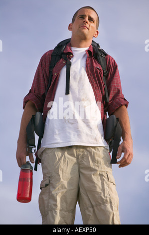 Ein Wanderer und Kletterer steht Ontop eines Berges halten Sie einen Wasserkrug und einen Rucksack trägt ein rotes Hemd und einem blauen Himmel Stockfoto