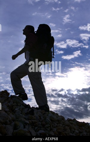 Niedrigen Winkel Blick auf ein erwachsener Mann auf einem Steinhaufen klettern. Er ist gegen einen blauen, bewölkten Himmel abhebt. Vertikale Schuss Stockfoto