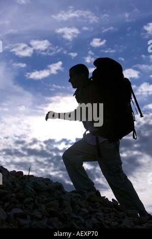 Niedrigen Winkel Blick auf ein erwachsener Mann auf einem Steinhaufen klettern. Er ist gegen einen blauen, bewölkten Himmel abhebt. Vertikale erschossen. Stockfoto