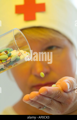 eine Pille, die Herausfallen aus einem Glas gefüllt mit Pillen in verschiedenen Farben und Formen nach unten auf eine geöffnete Hand im Hintergrund eine Krankenschwester Stockfoto
