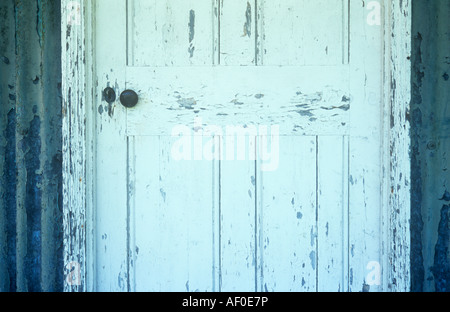 Detail der Holztür mit Abplatzungen weiße Farbe und alte Türklinke inmitten einer Wellpappe Aluminium Wand mit abblätternde Farbe olive Stockfoto