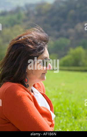 Frau sitzt auf dem Rasen in der Sonne mit Hügeln hinter Stockfoto