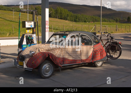 Citroen 2CV-Auto an der schottischen Tankstelle, maßgeschneidert, französische Touristen, individuelle Stoffumhüllung, drapiert mit schottischem Kilt Schottland UK Stockfoto