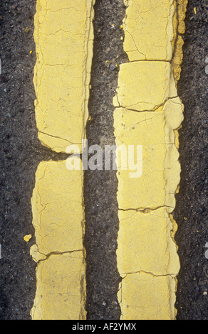 Detail aus direkt oberhalb von gerissenen und blass gelbe Doppellinien übermalt viermal auf getragen graue Asphaltstraße Stockfoto