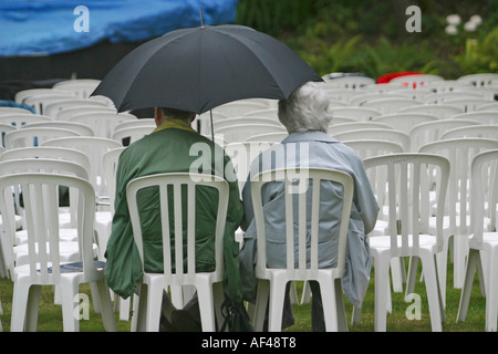 Ein älteres Ehepaar sitzen unter einem Regenschirm im Regen warten auf die Oper im alten Pfarrhaus zu starten Stockfoto