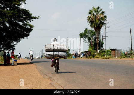 Schwarze Afrikaner, die schwer beladenen Fahrrad fahren entlang der Straße Maseno Kisumu in Western Kenia in Ostafrika Stockfoto