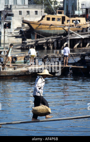 Lokale Arbeiter trägt schweren Last von einer Dschunke über schmale Brett über Wasser mit traditionellen Joch auf Peng Chau Insel Hong Kong Stockfoto