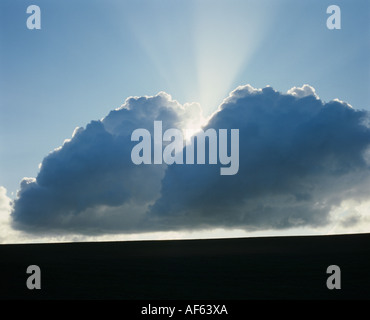 Sonne hinter Cumulus-Wolken mit Sonnenstrahl gegen blauen Himmel Stockfoto
