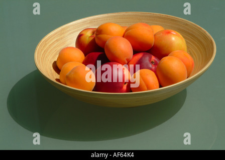 Schale aus Bambus, gefüllt mit Aprikosen und Nektarinen auf grünem Glas Hintergrund gemacht Stockfoto