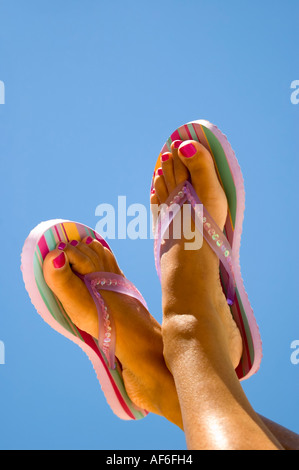 Vertikale Nahaufnahme von einer Frau gebräunte Füße mit lackierten Zehennägeln tragen gestreifte gegen ein strahlend blauer Himmel Flipflops Stockfoto