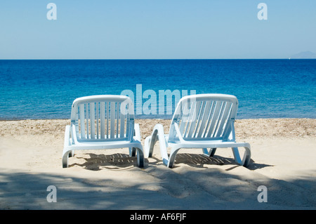 Horizontale Ansicht von zwei leeren Sonnenliegen auf einem tropischen weißen Sandstrand. Stockfoto