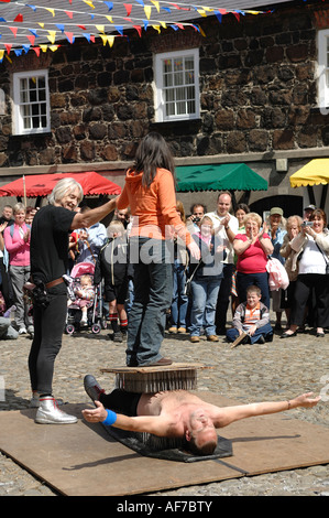 Performer, liegend auf einem Bett aus Nägeln mit einem Mitglied des Publikums stehen auf seiner Brust Lughnasa Messe Carrickfergus Castle Stockfoto