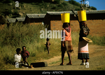 Zwei schwarze Frauen Wasser in leuchtend gelben Eimer auf dem Kopf tragen. Östlichen Freistaat; Südafrika Stockfoto