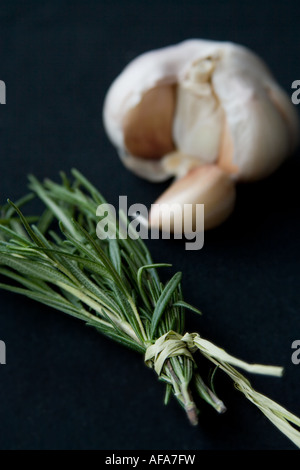 Knoblauch und einem gebundenen Rosmarinzweig auf einem schwarzen Hintergrund. Stockfoto