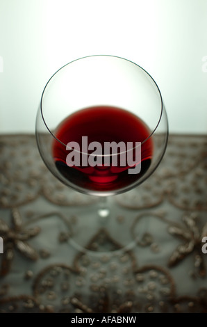 Weinglas mit Rotwein auf einer Perlen Tischdecke teilweise gefüllt. Der Hintergrund ist hell erleuchtet. Stockfoto