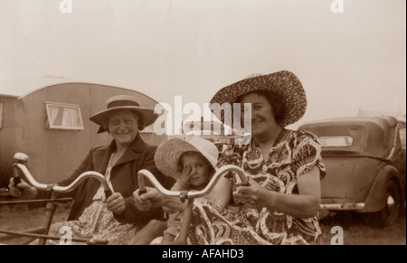 Originales lustiges Foto von Frauen, einem kleinen Kind, das auf Fahrrädern fährt und Spaß im Freien während eines Caravaning-Urlaubs in Großbritannien der 1940er Jahre hat Stockfoto